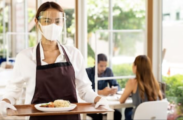 Portrait attractive asian waitress wear face mask and face shield holding food tray to serving meal to customer with custome in background