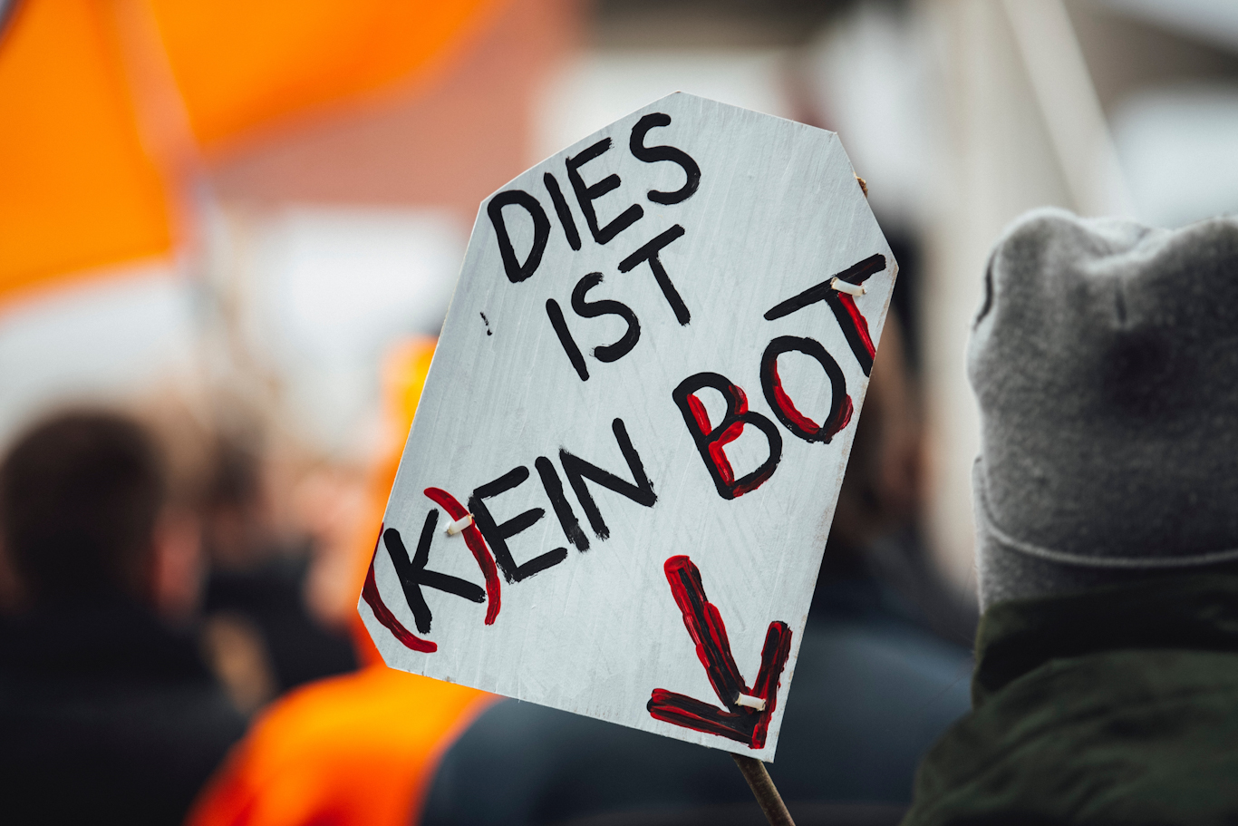 A protest sign that reads "Dies ist (K)ein Bot" with an arrow pointing down