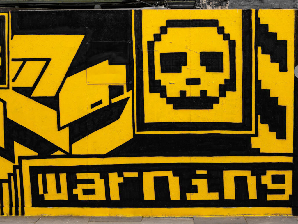 Yellow and black graffitti of skull, internet files, and warning sign