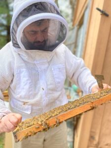 Posse cares for his bees while dressed in white protective equipment including a face covering. 