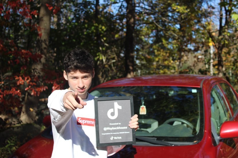 man holds tiktok plaque from TikTok in front of a red car