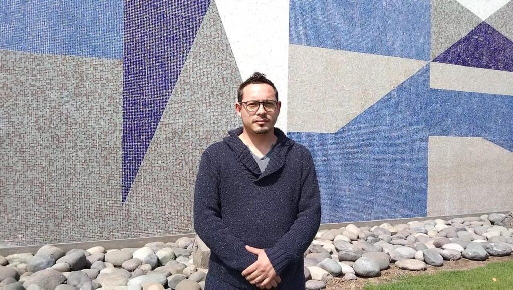 Francisco Torres in front of San Ignacio El Bosque’s facade, a colorful blue, grey and white geometrical mosaic.