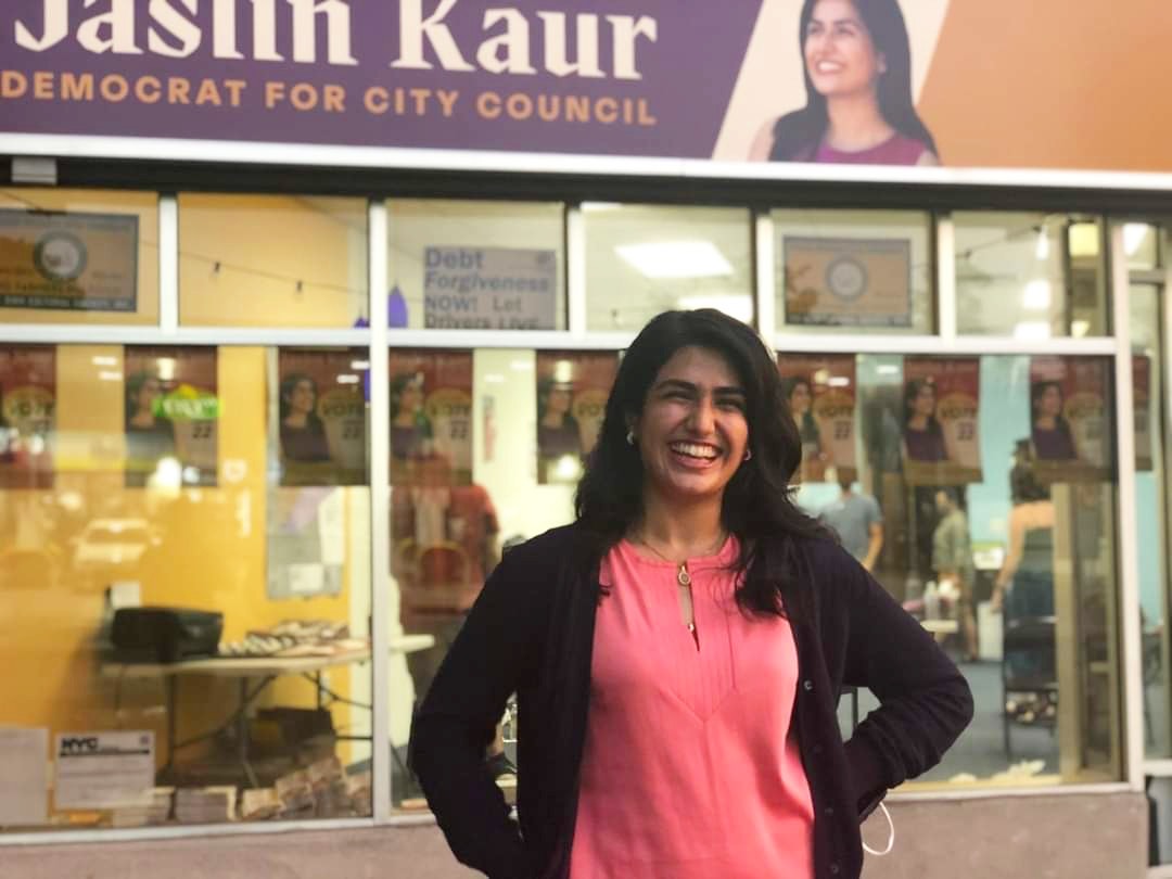 Jaslin Kaur standing outside her campaign office, in front of a sign that reads "Jaslin Kaur: Democrat for City Council".