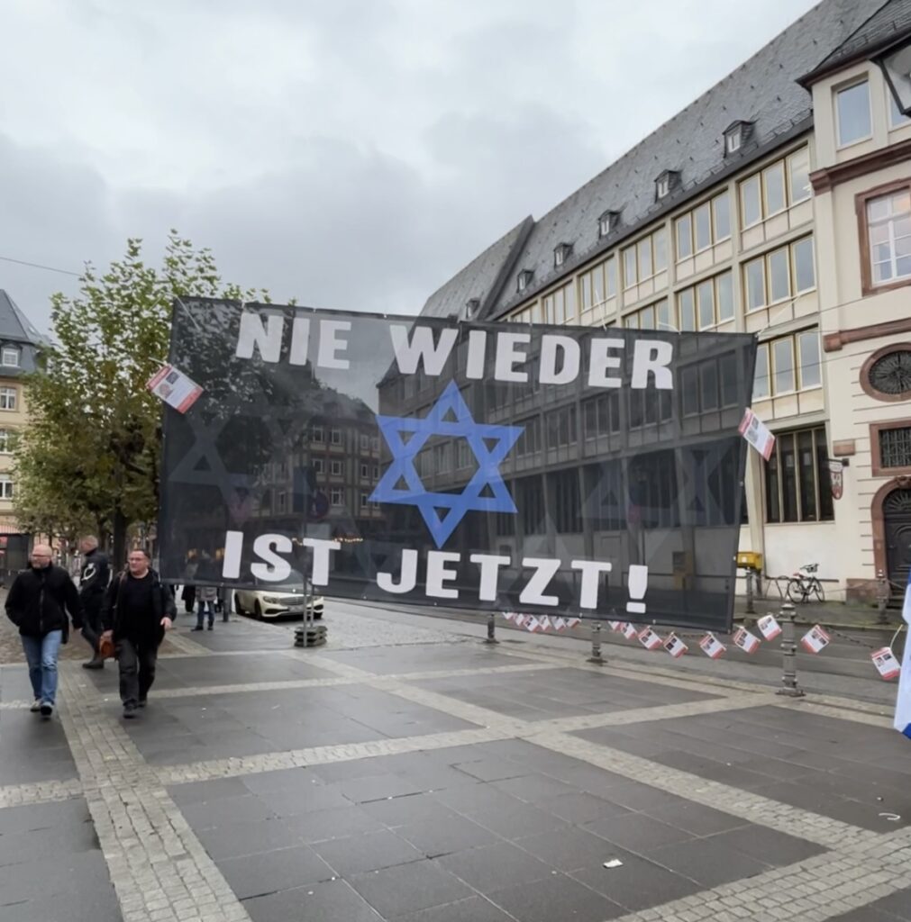 Sign with a star of David in German reading "Nie wieder ist jetzt!" which translates to "never agains is now!"