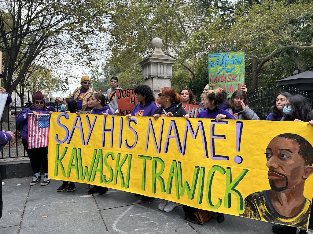 Community organizers hold a banner that reads "Say his name! Kawaski Trawick"