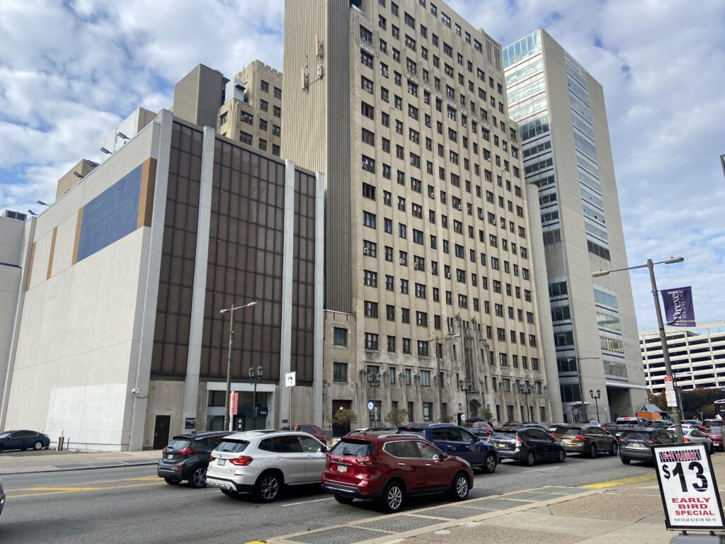 Cars drive in front of a multistory rectangular urban building.