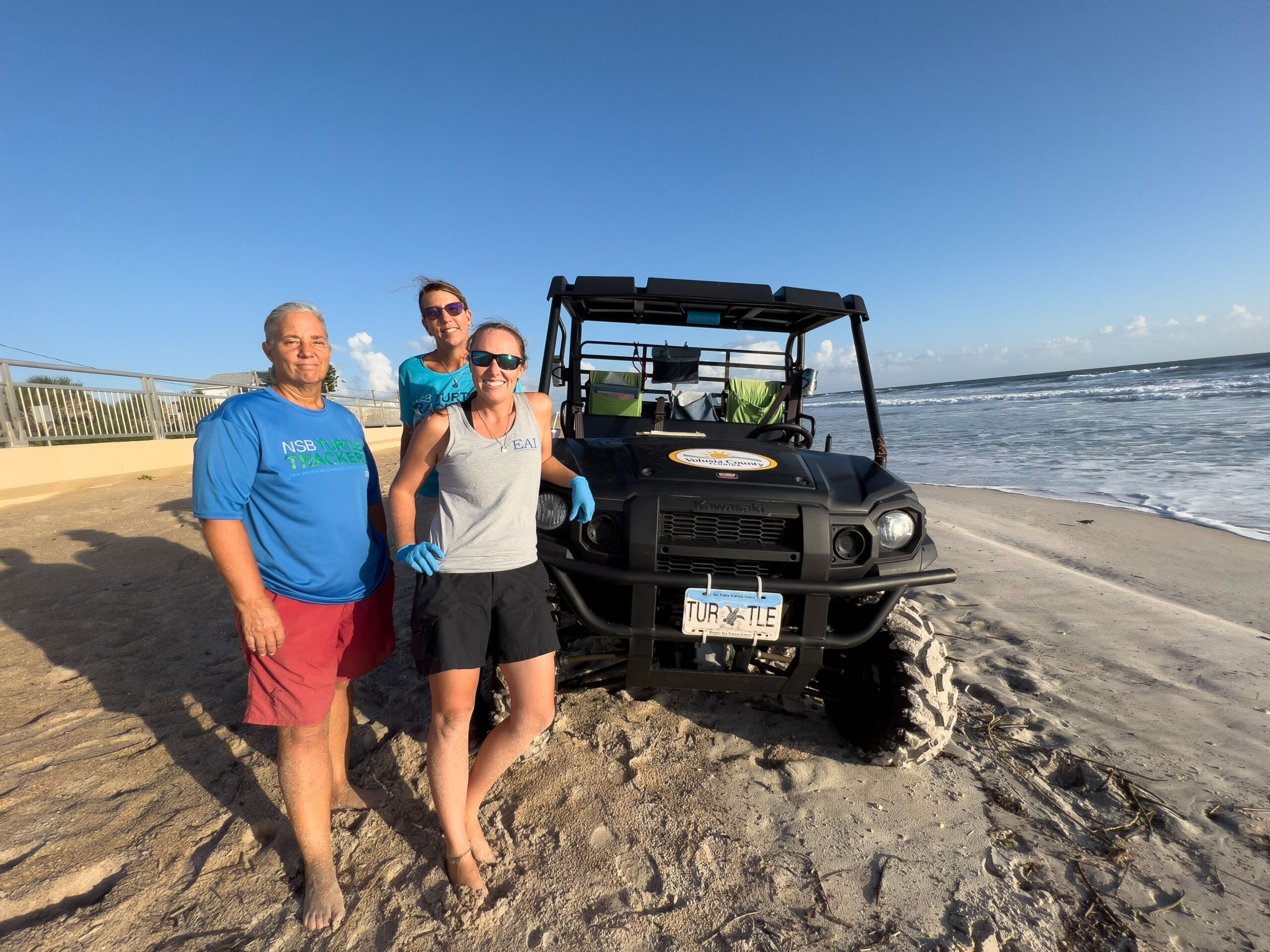 Biologist Jaymie Reneker (right), Jennifer Winters, protected species manager for Volusia County (center), and volunteer Jean Callaghan (left) pose in front of their all-terrain vehicle while on their morning rounds monitoring sea turtle nests in New Smyrna Beach, Florida. (Credit: Jennifer Taylor)