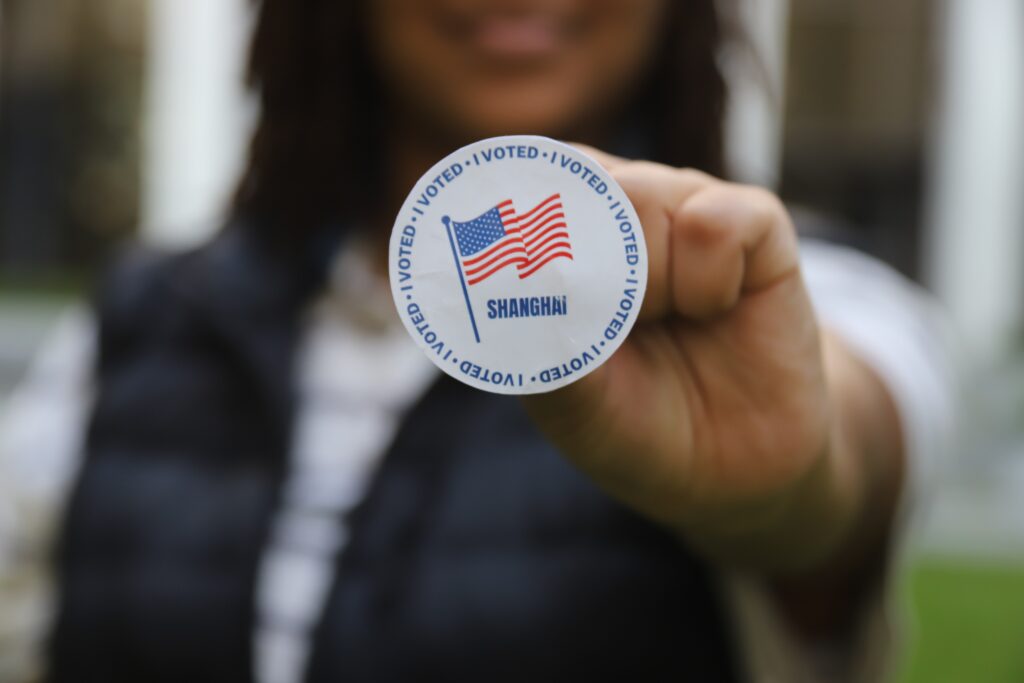 an American in China holds an "I voted" sticker