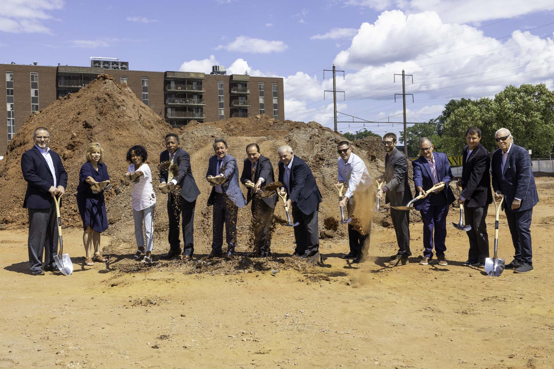 A group of city officials and developers with shovels pose in front of large mounds of dirt at the groundbreaking ceremony for the OneWest development in Linden, NJ.