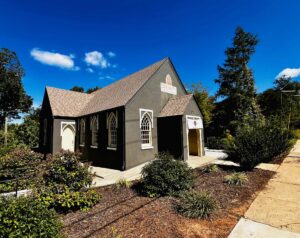 The exterior of the Titled Map, a black one-story building with several gothic-arched windows and a sidewalk leading to the front entryway.