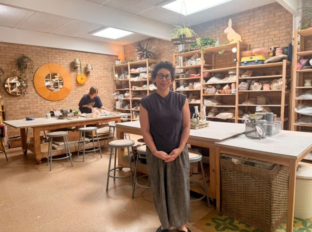 Co-Owner Jane Parsons standing inside Pottery for the People with instructor Charlotte working in the background