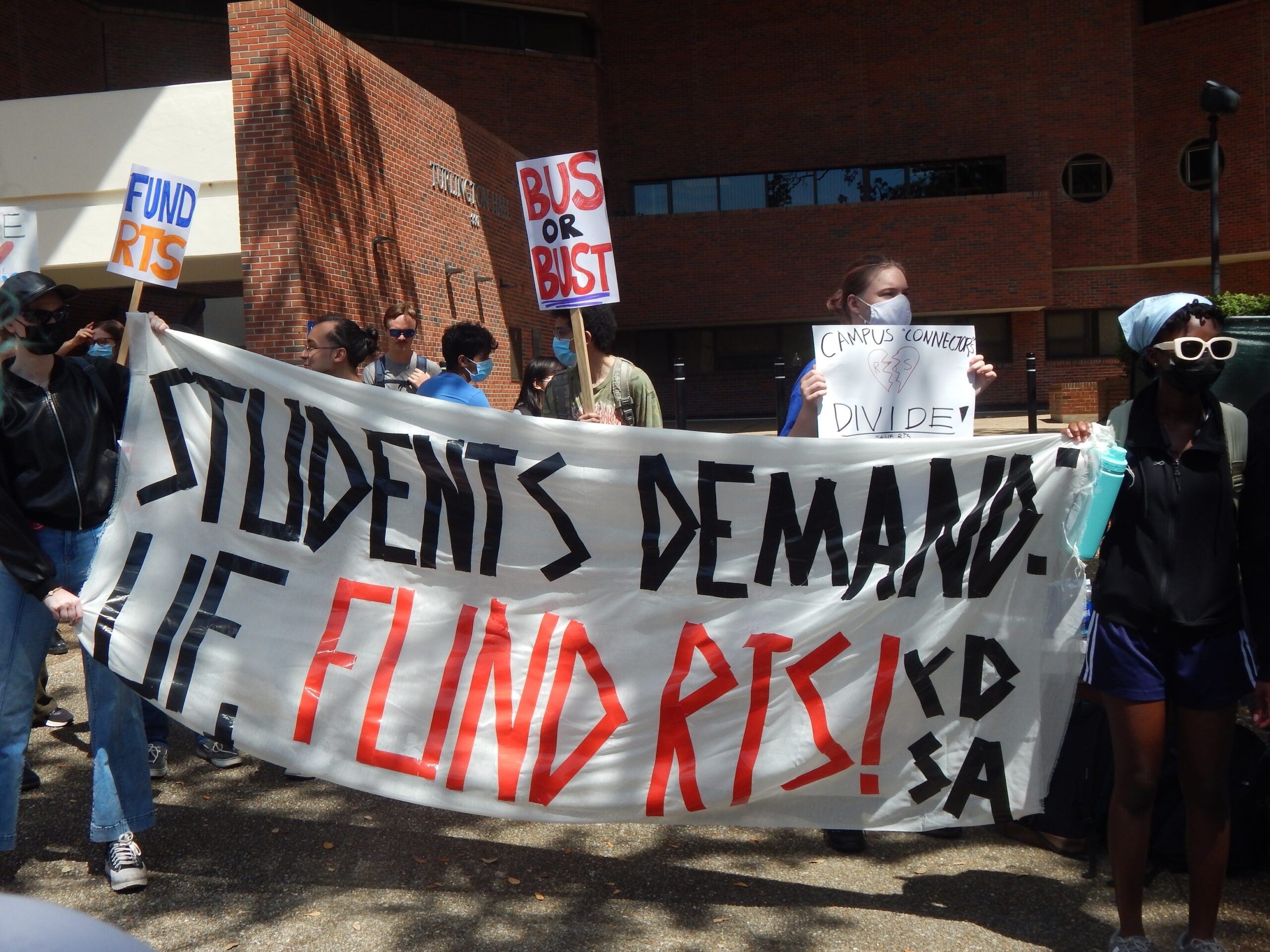 Students hold a banner that says "Students Demand. UF, Fund RTS"