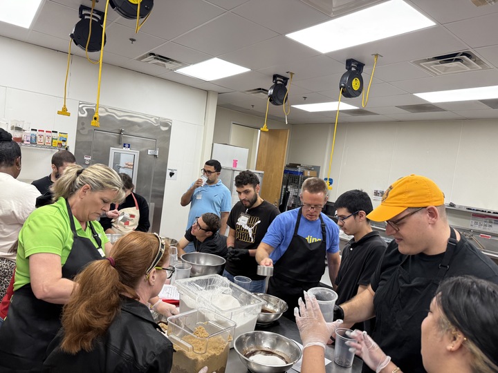 Newly hired Hugs Cafe employees gathered around prep table making brownies