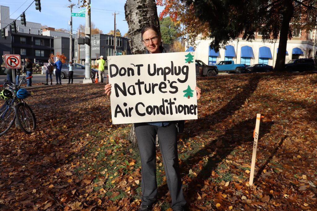 Woman holds sign in front of tree