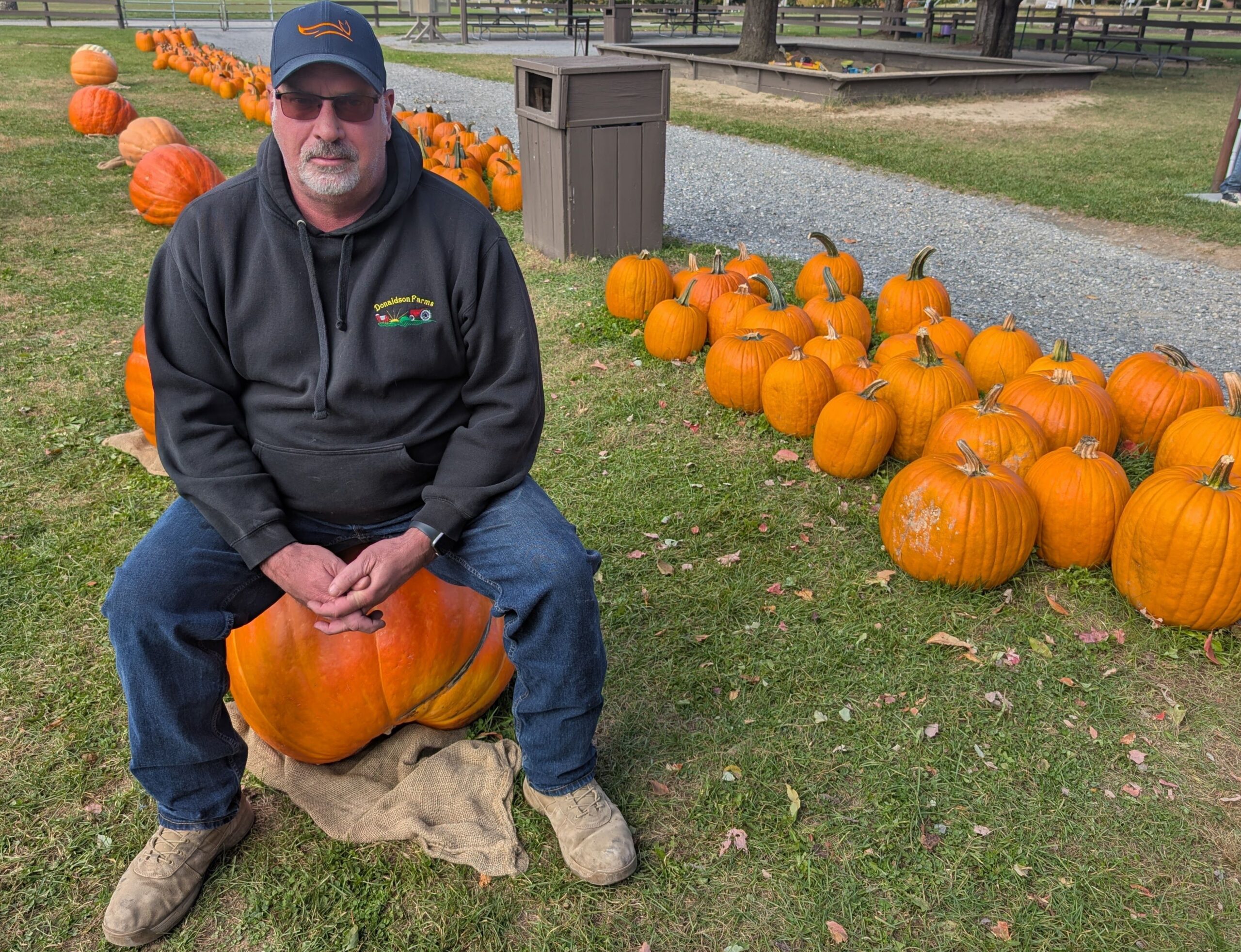 A farmer seated on a large pumpkin.